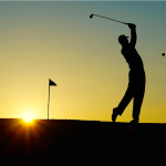 Shadow of golfer hitting ball with sunset behind