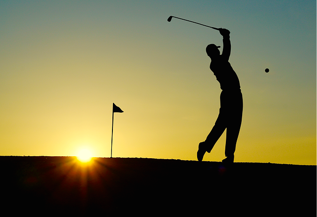 Shadow of golfer hitting ball with sunset behind